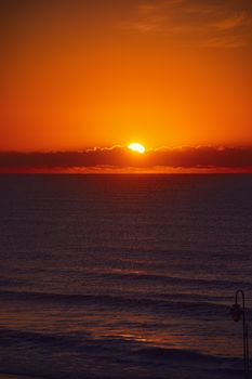 A vibrant sunset over the tranquil sea with dramatic skies and a glowing horizon.