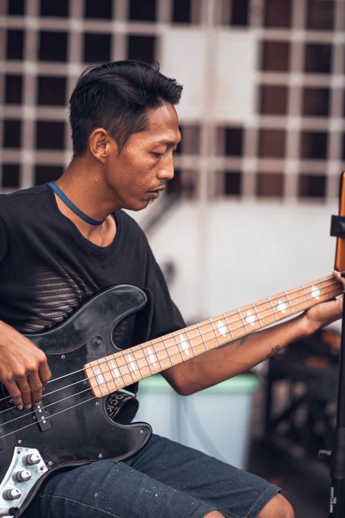 Free A musician intensely playing an electric bass guitar, captured in a vertical shot. Outdoor setting. Stock Photo