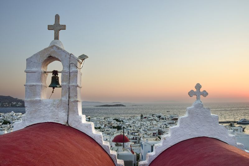 Serene sunrise view over Mykonos with iconic church domes against the sea.