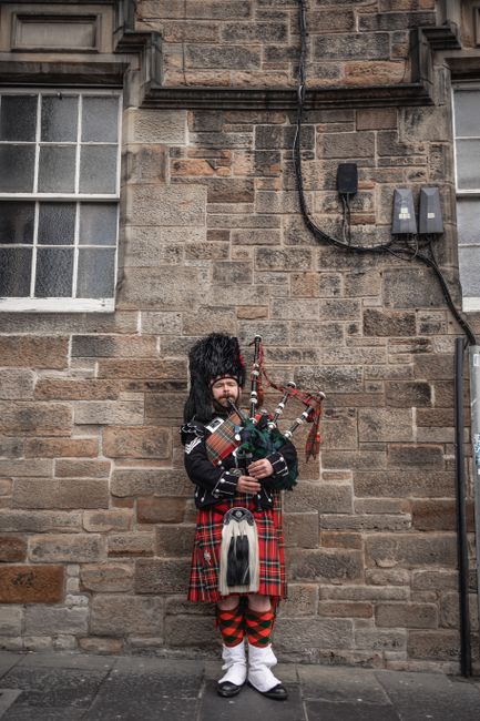 Traditional Scottish bagpiper in kilt playing on city sidewalk.