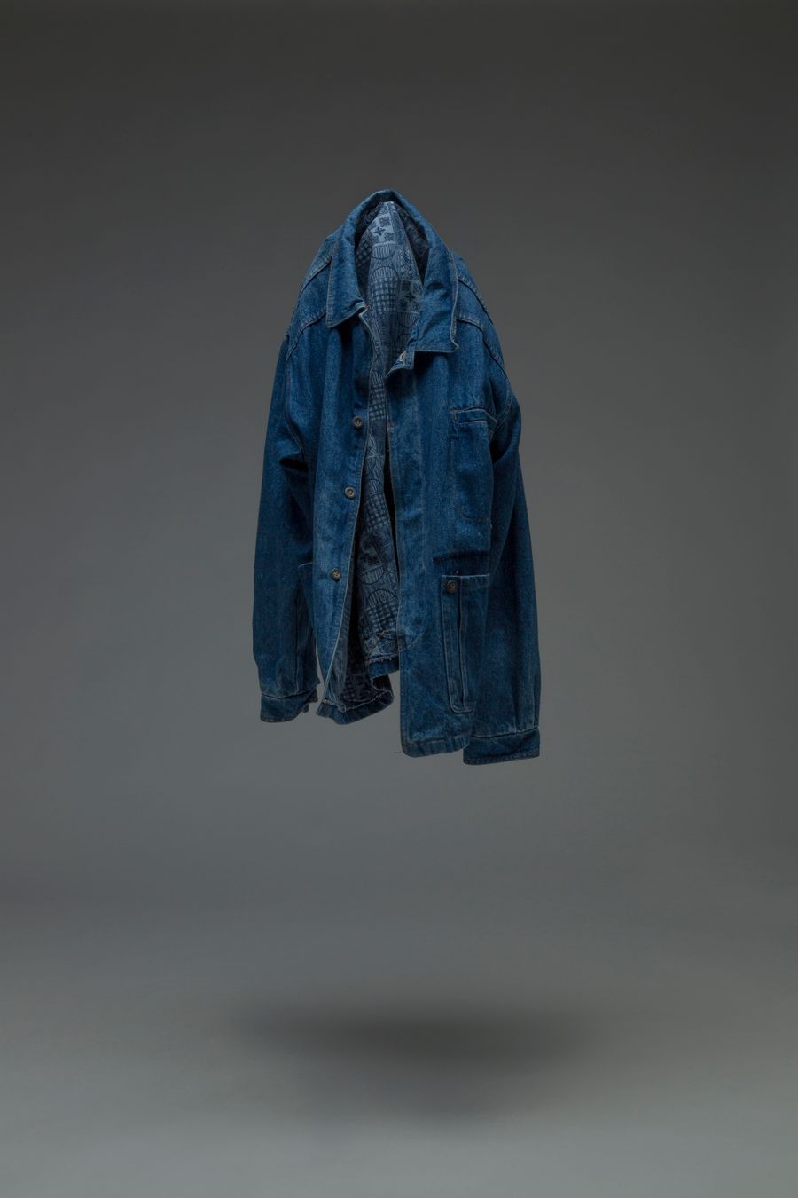 Denim overshirt suspended against a grey studio wall — photo by James Frid on Pexels