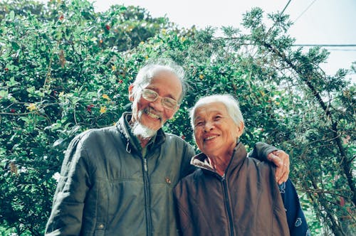Elderly man and woman smiling together, with man's arm around his woman