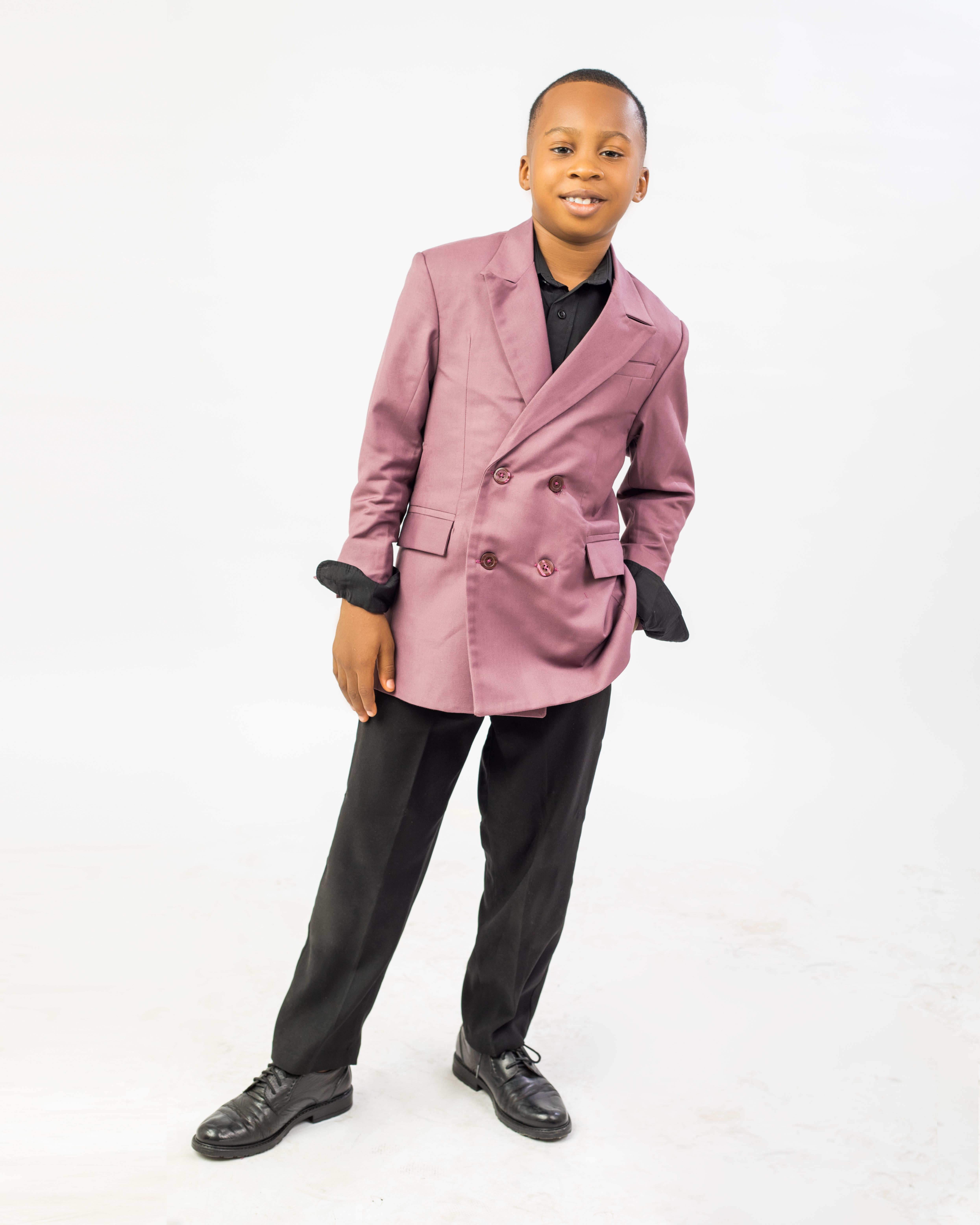 Charming young boy posing confidently in a pink suit on a white background, exuding fashion and joy.