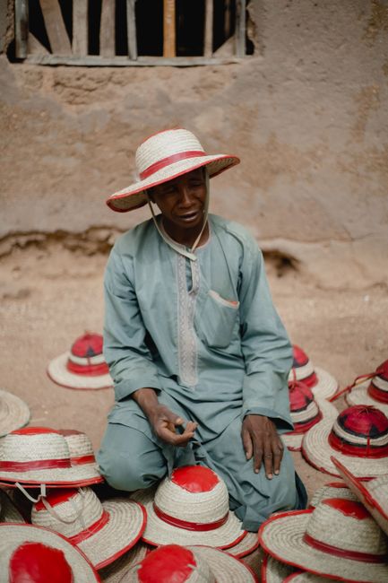 Nigerian man selling handmade hats in a local market. Authentic cultural scene.