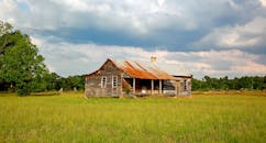 天空多云，一座风化的农舍矗立在生机勃勃的田野中