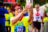 一位面带微笑的资深女士在充满活力的户外马拉松比赛中自拍，为比赛日增添了欢乐