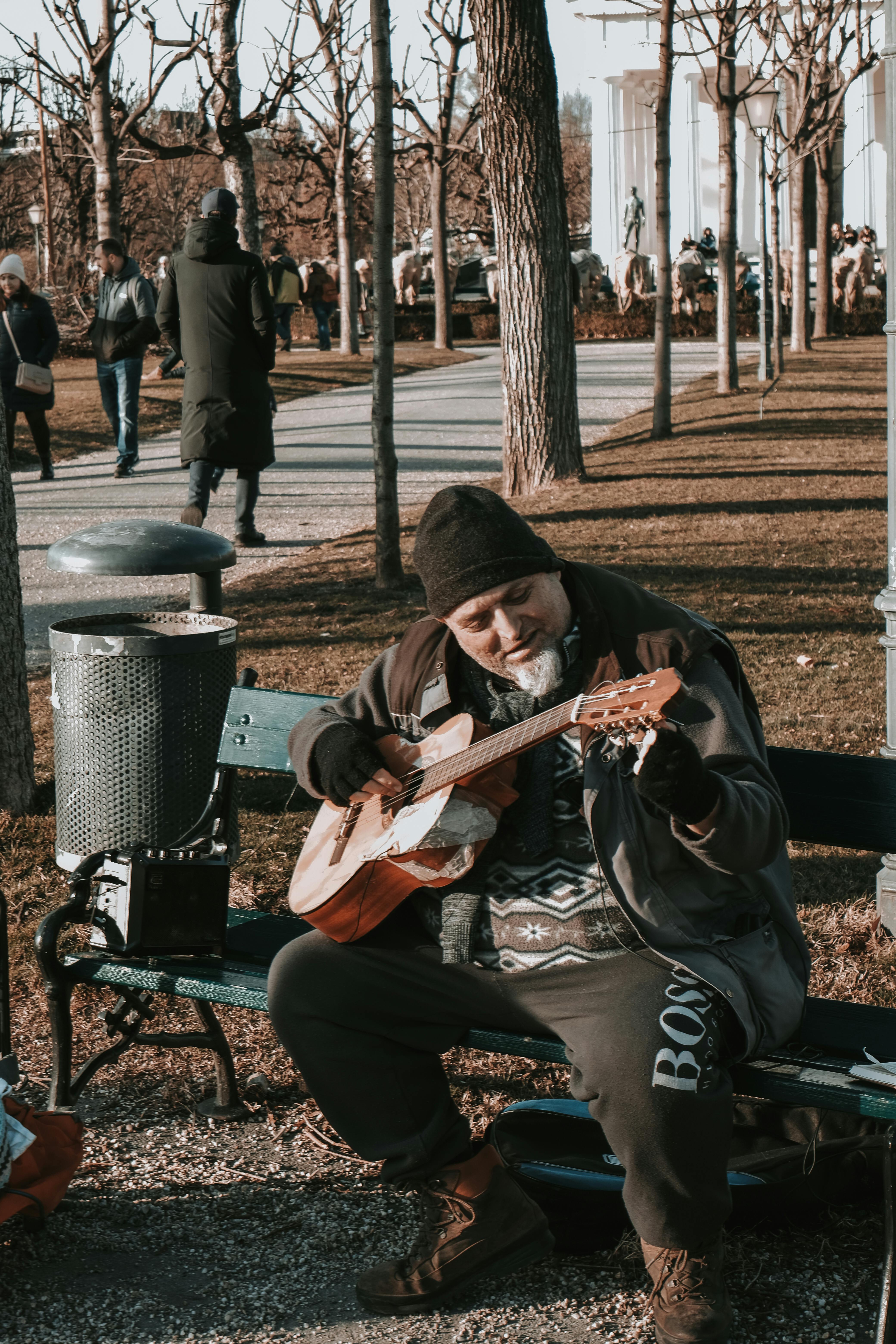 a man playing guitar on a bench in a park