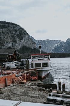 Serene winter scene of a boat docked by a lakeside village amidst snow-capped mountains.