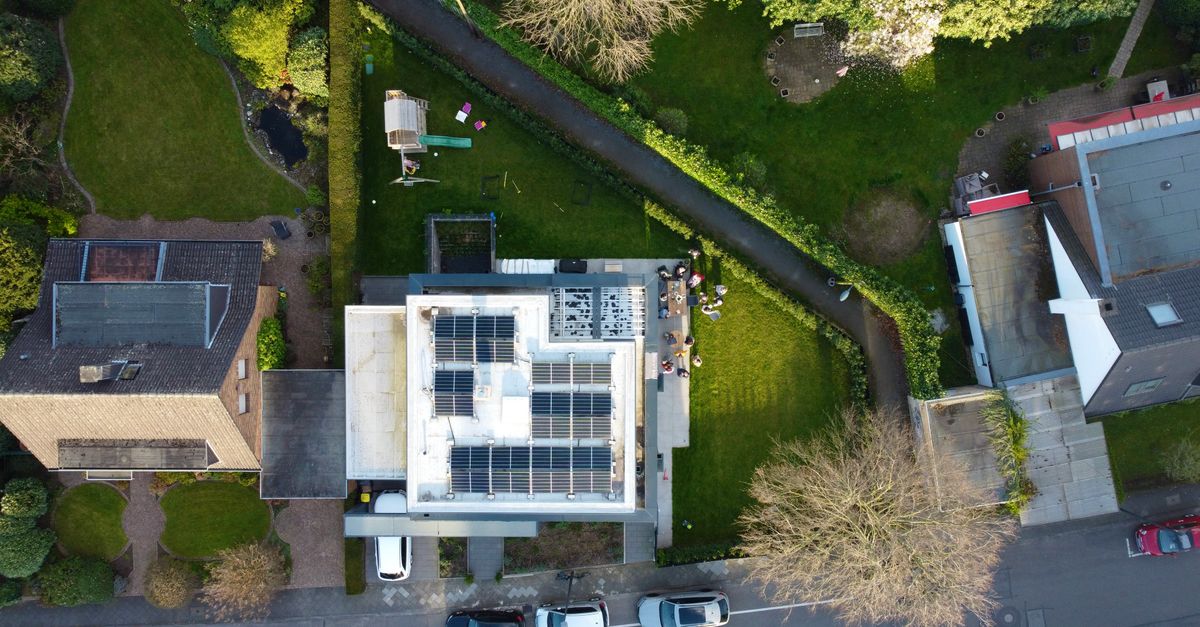 Aerial view of suburban houses featuring solar panels on rooftops and green gardens.