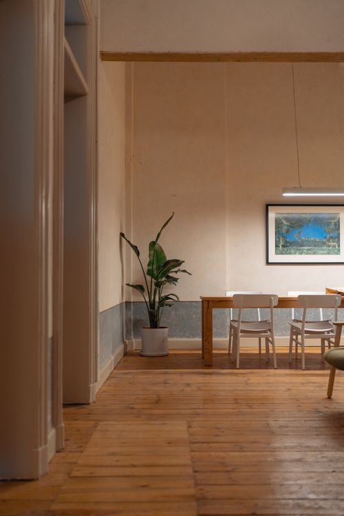 Free Warm dining room scene featuring wooden floors, chairs, a potted plant, and wall art. Ideal for interior design themes. Stock Photo