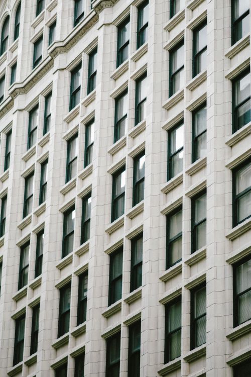 Free Close-up of a classic urban building facade featuring multiple windows and elegant architectural details. Stock Photo