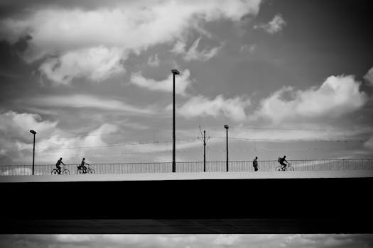 在戏剧性的天空下，人们骑着自行车走过一座桥，构成了一幅迷人的黑白图像