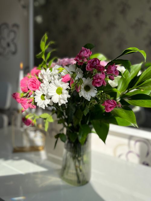 Free Beautiful bouquet with pink roses and white daisies in a glass vase on a sunlit table. Stock Photo