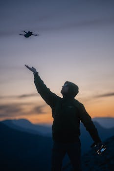 A captivating silhouette of a man flying a drone at twilight with a stunning sunset background.