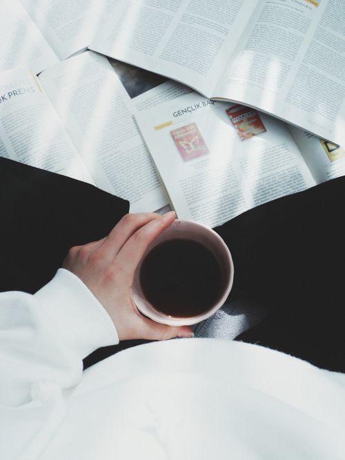 Free A person enjoys a cup of coffee while sitting with open magazines in a cozy setting. Stock Photo
