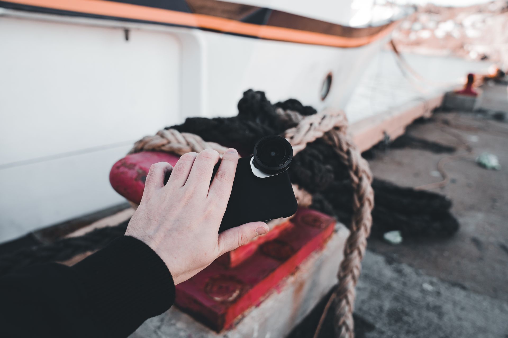 A hand holding a smartphone with fisheye lens by the harbor, showcasing technology and travel.