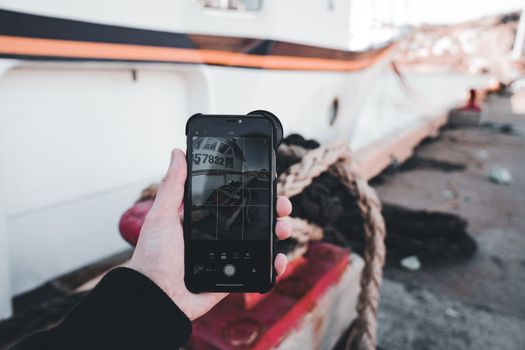 A person photographing a moored ship with a smartphone, emphasizing technology and travel.