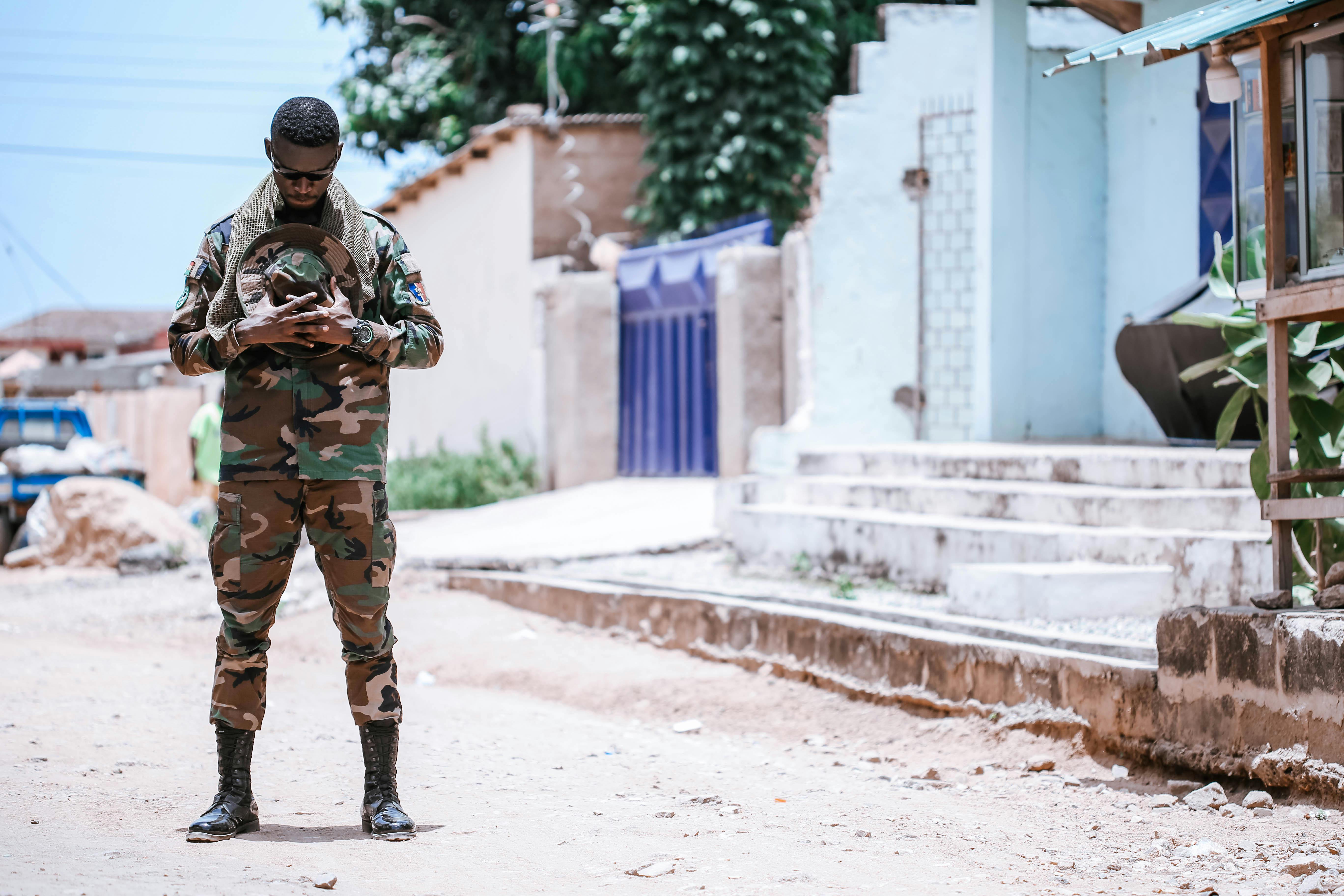 Military soldier in camouflage uniform standing in a sunny urban environment.