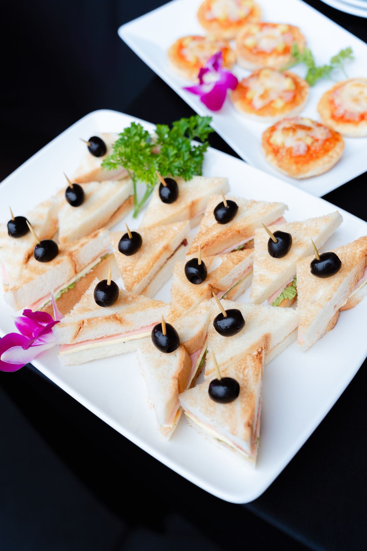 Mini sandwiches and pinwheels garnished with olives and parsley on a platter