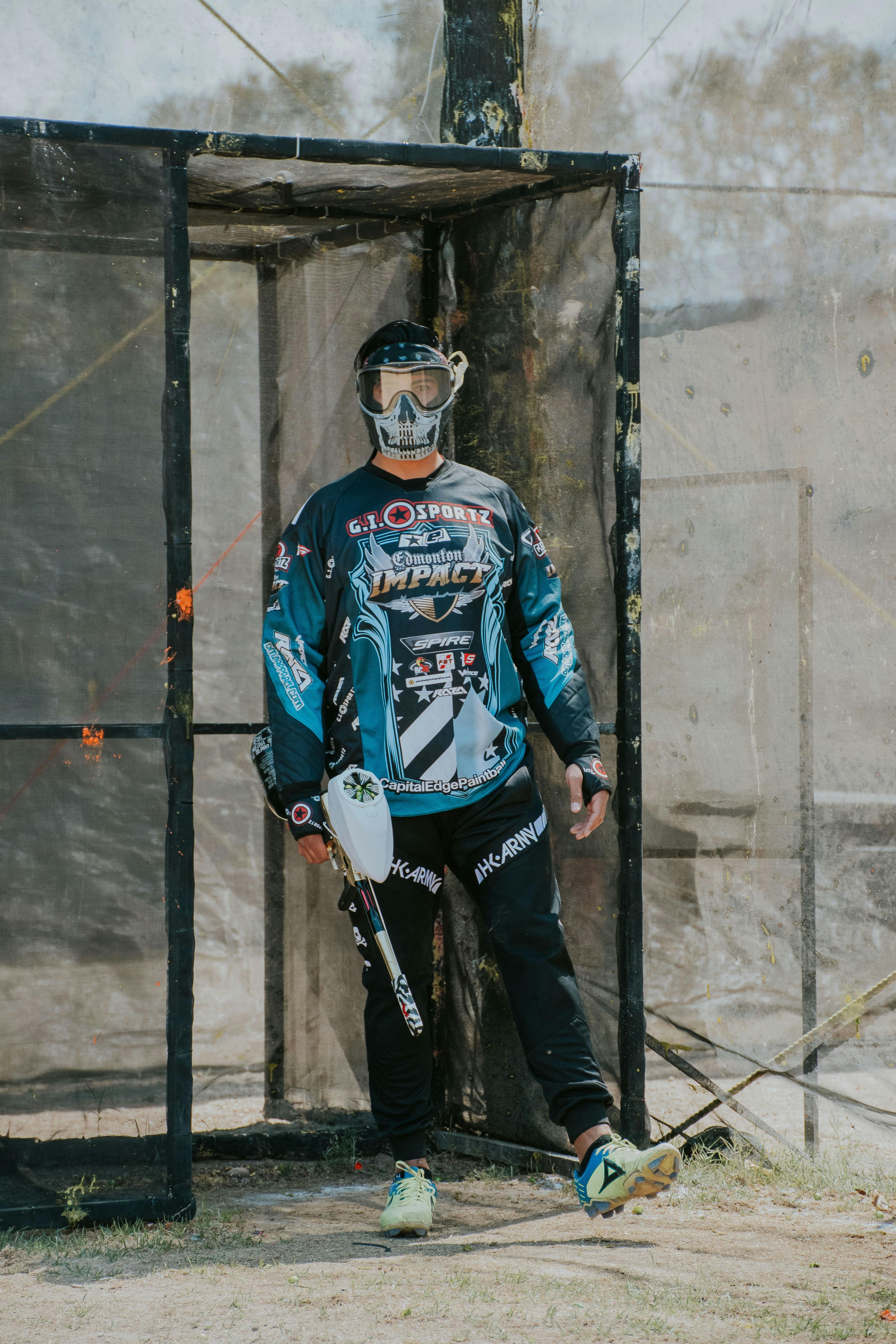 Un homme en tenue de paintball se tient prêt avec un masque et un fusil par une journée ensoleillée. Prescription Goggle Inserts - A man in paintball gear stands ready with mask and rifle on a sunny day.