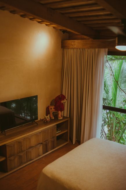 Fotomural Dormitorio cálido y acogedor con una decoración de madera, televisión y vista de la ventana hacia la vegetación.