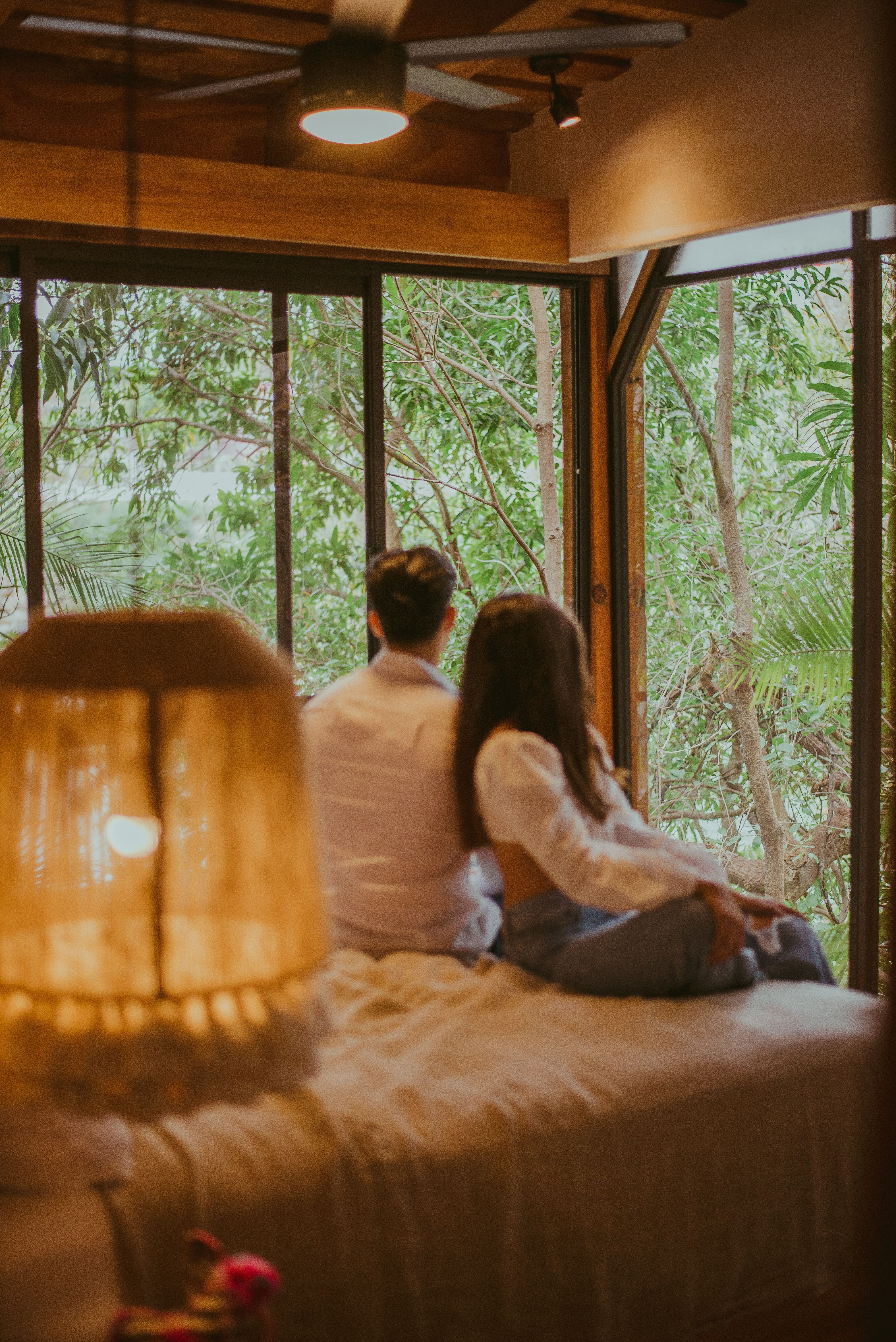 A couple sitting by a wide window in a timber bedroom looking out over the trees. Photo by Luis Zambrano on Pexels.