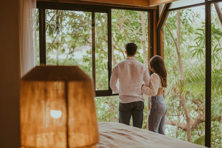 Couple Looking Through Window In Bedroom