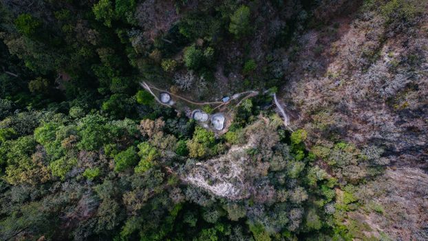 Drone shot capturing a lush green forest with visible storage tanks from above.
