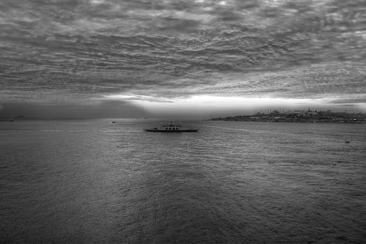 A serene black and white view of the Bosphorus Strait with a ship at dusk, showcasing Istanbul's skyline.