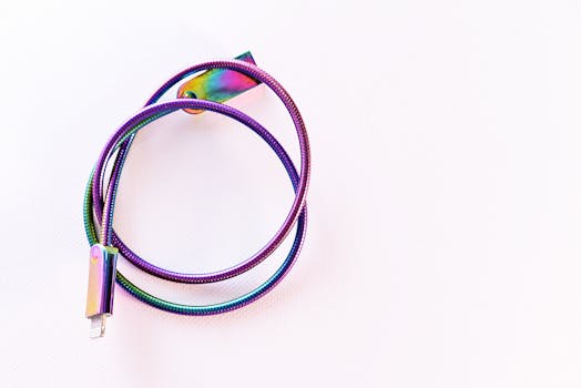 A vibrant, rainbow-colored USB cable coiled on a bright white surface. by Diana ✨