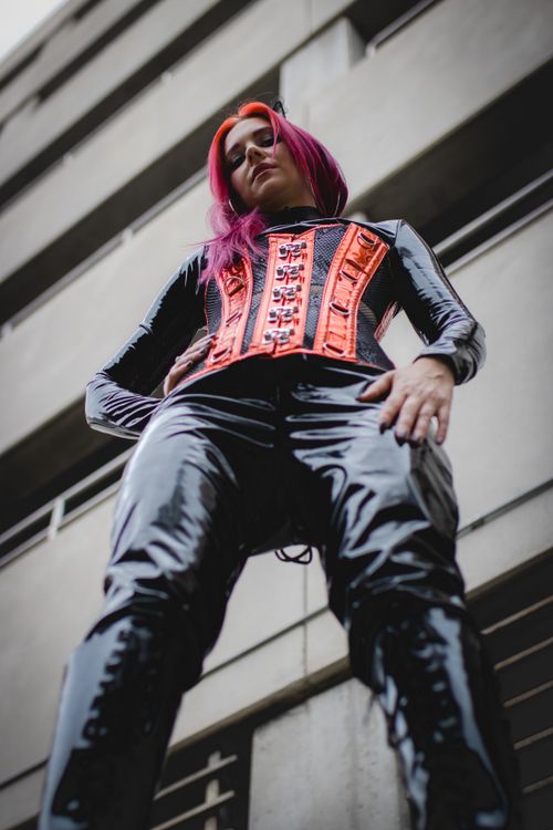 Free Low angle shot of a young woman in a striking outfit against a building facade, showcasing the urban lifestyle. Stock Photo