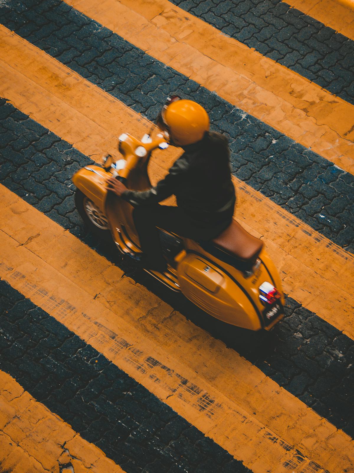 Person riding a yellow motor scooter across a zebra crossing in city traffic