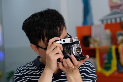 Free Man with glasses capturing a photo using a vintage camera indoors. Stock Photo
