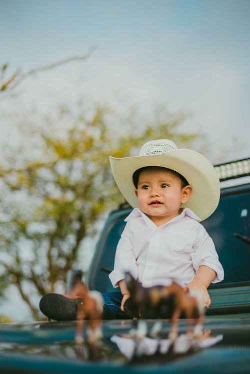 A Little Boy in a Cowboy Hat Sitting on a Car Hood 