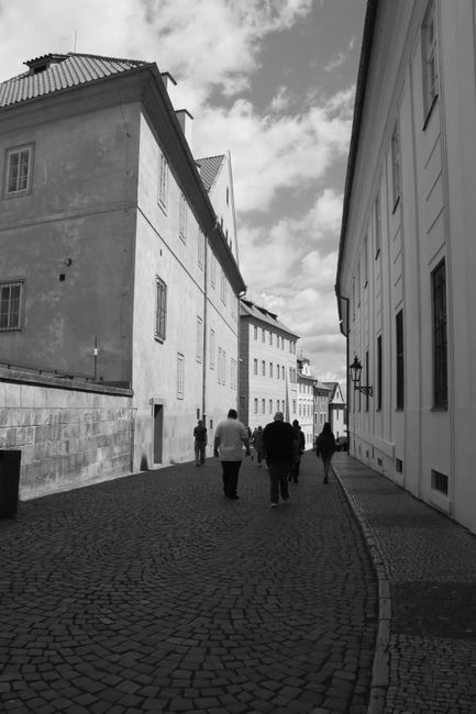 Black and white photo of people walking on a cobblestone street in Prague.