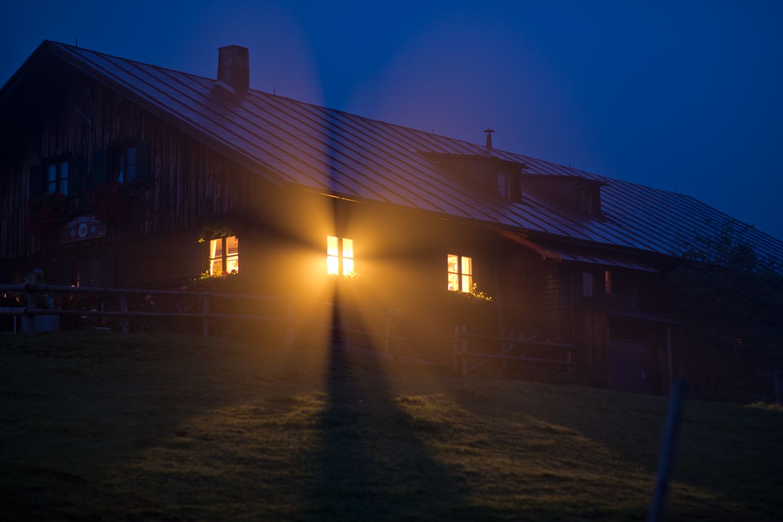 The house at Nāra at the blue hour, upstairs windows lit warm against a deep indigo sky