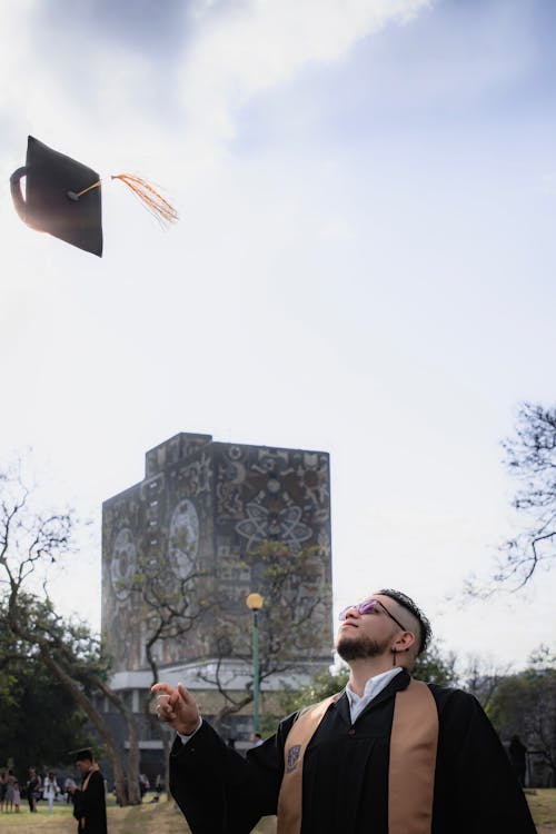 Man Wearing a Graduation Gown Tossing the Mortarboard in front of the University of Mexico