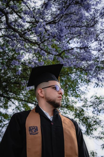 A young man in graduation attire stands under a blooming spring tree, reflecting academic achievement. A young man in graduation attire stands under a blooming spring tree, reflecting academic achievement.