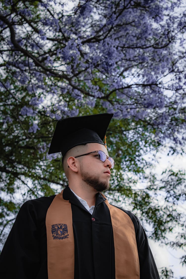 Young Man Wearing A Graduation Gown And A Mortarboard Standing Outdoors 