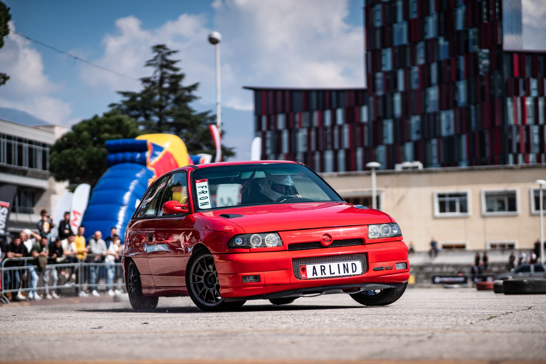 Dynamic capture of a red Opel Astra drifting at an urban car event.