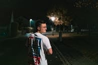 夜晚，一名年轻人走在灯光昏暗的街道上，营造出神秘的城市氛围