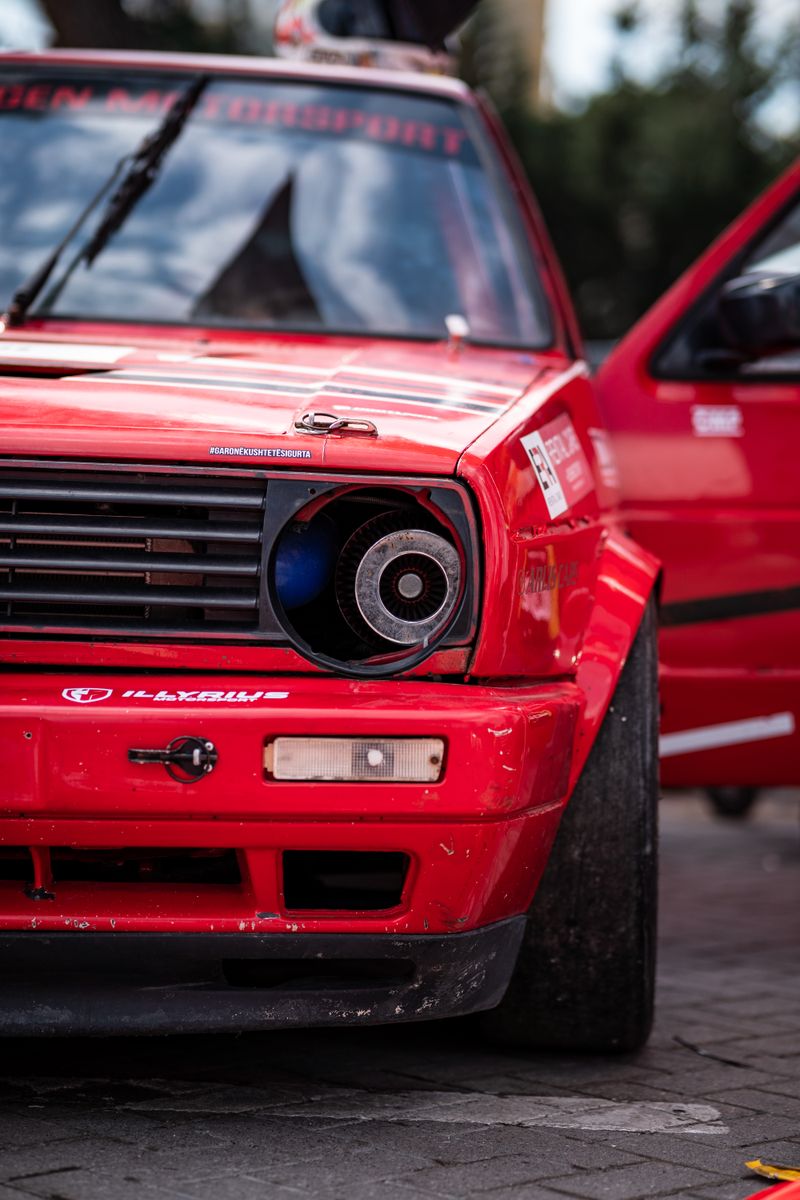 Close-up of a red Volkswagen Golf II showcased at a car event, highlighting its sporty design.