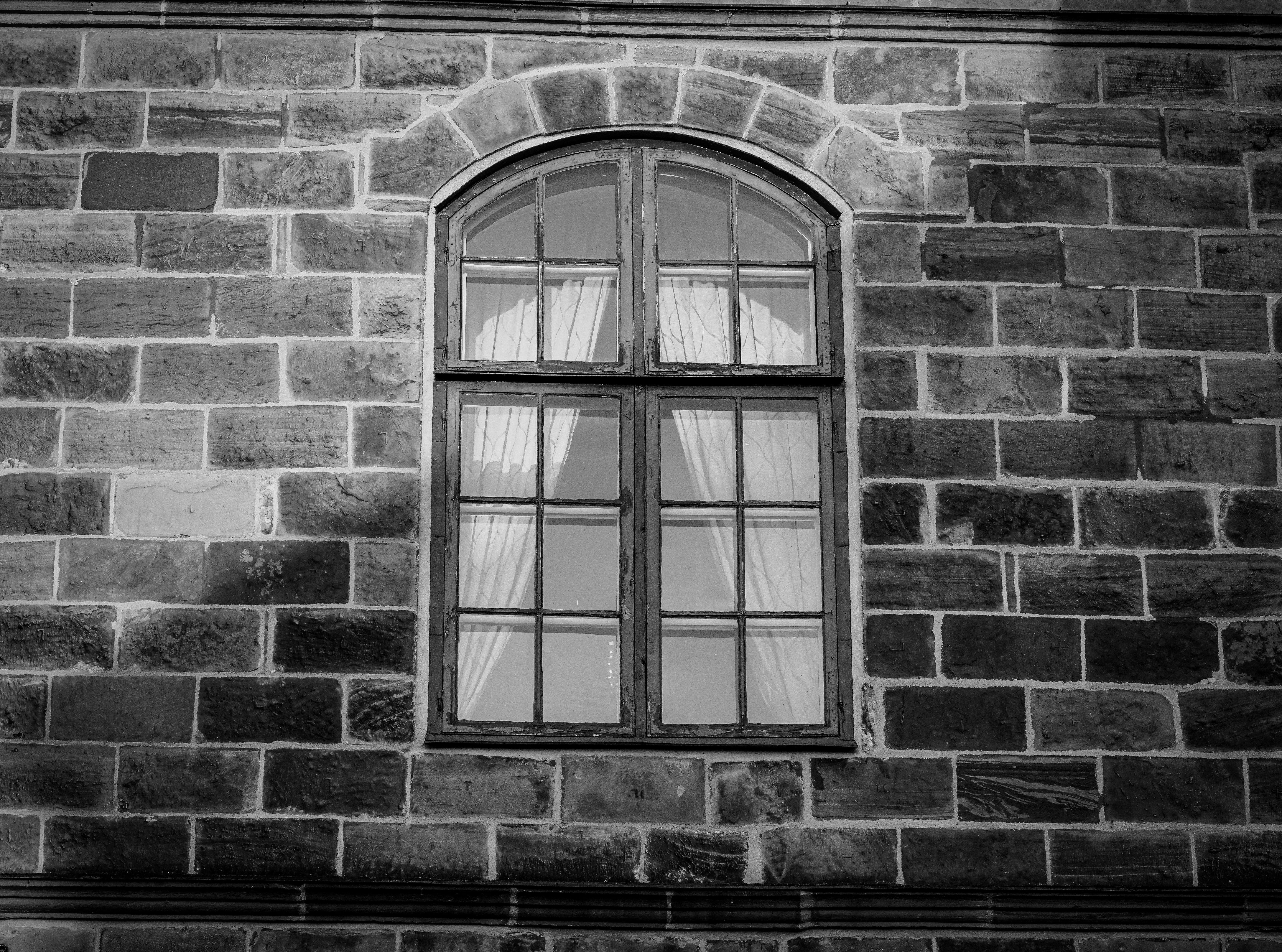 Elegant black and white image of an arched window on a classic brick facade, showcasing historical architecture