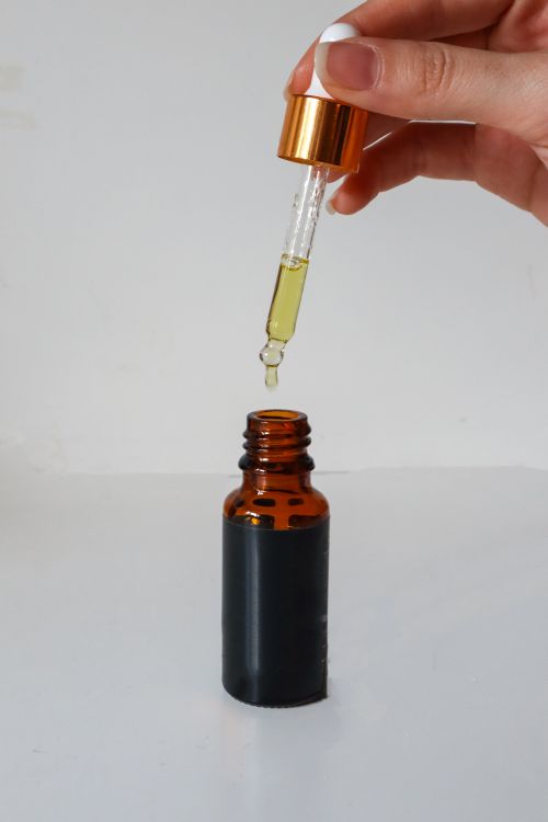 Free A hand holds a dropper releasing liquid into an amber vial on a white background, symbolizing precision and care. Stock Photo