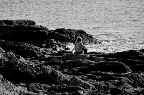 Free A woman sitting on eroded rocks by the sea shore, in black and white. Stock Photo