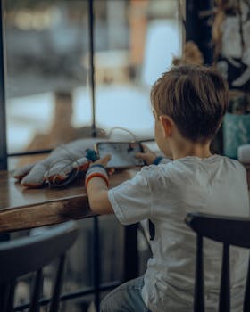 Young boy engrossed in a mobile game at a wooden table inside a cozy room.