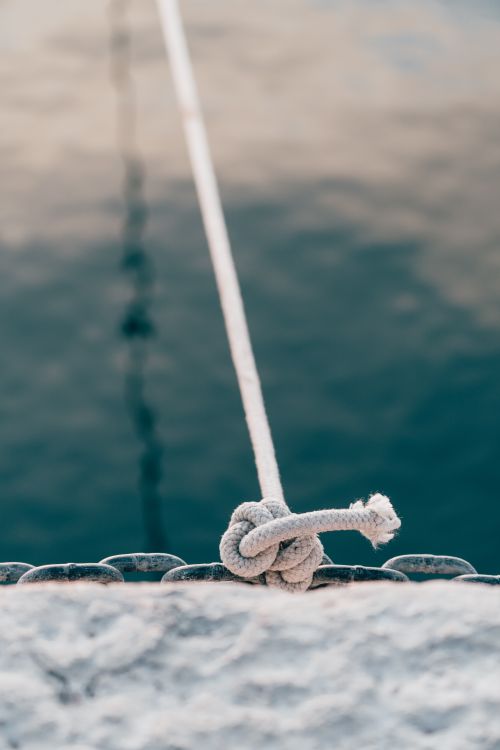 Free Close-up of a rope tied above tranquil water, showcasing texture and reflection. Stock Photo