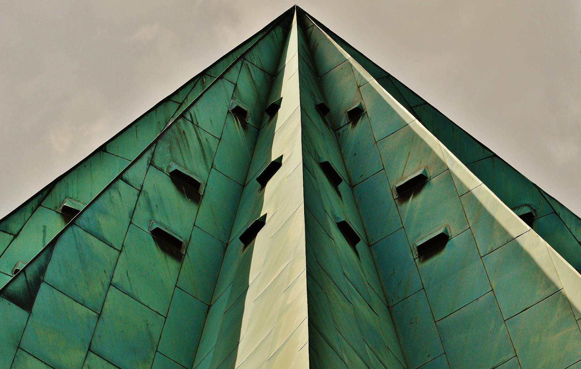 A striking low-angle view of a green metal-clad building with geometric lines and moody sky.