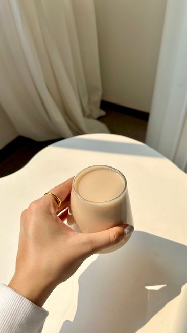 Cách Nấu Sữa Macca Úc Thơm Béo Mịn, Không Bị Lợn Cợn 3 A hand holding a glass coffee cup on a sunlit table, showcasing simplicity and elegance.