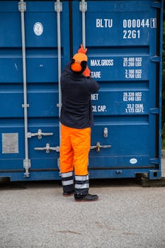 Industrial worker securing a shipping container outdoors, highlighting safety and logistics.